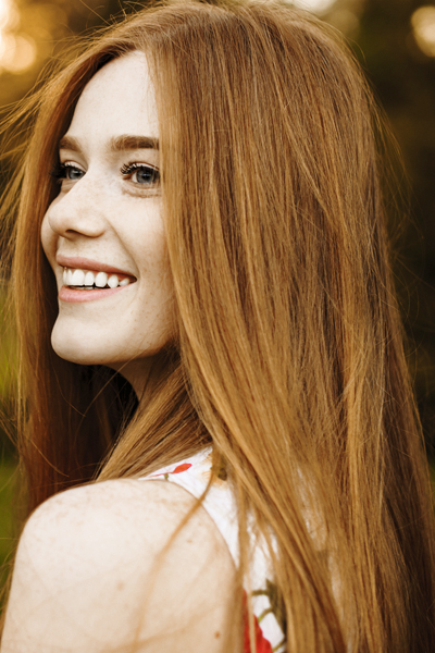 Portrait of a lovely female with long red hair and freckles looking away laughing against sunset outside
